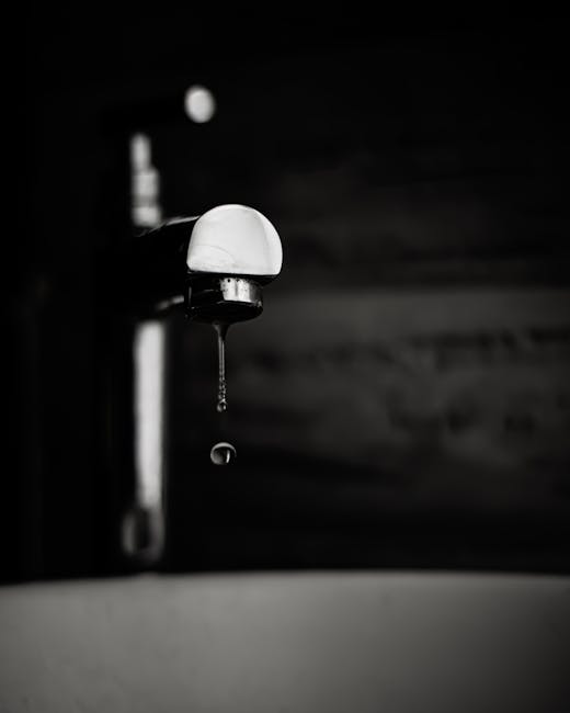 A striking black and white image capturing a water drop falling from a faucet, highlighting texture and contrast.